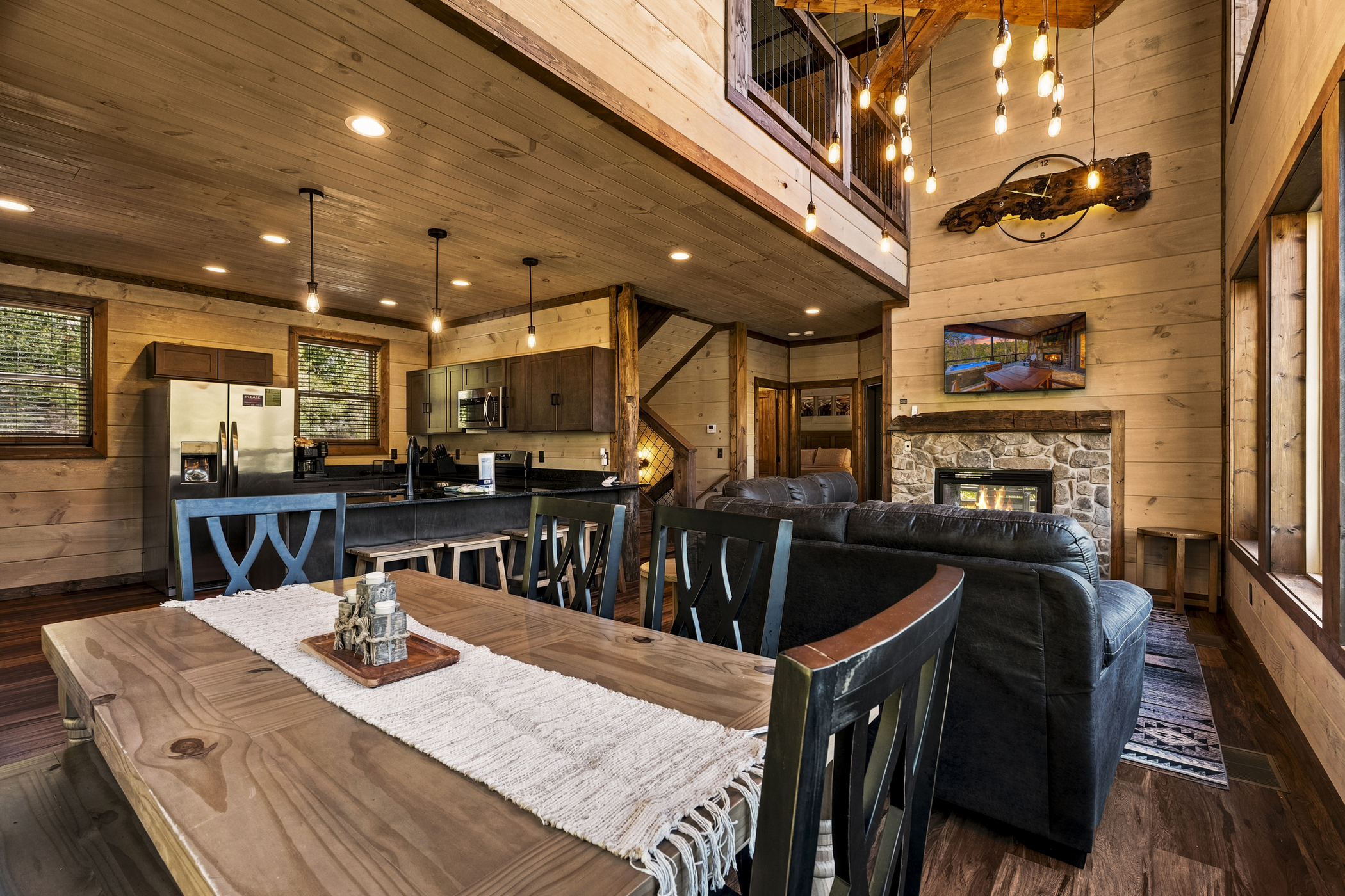 Warm timber cabin living and dining area with an illuminated stone fireplace and open kitchen.