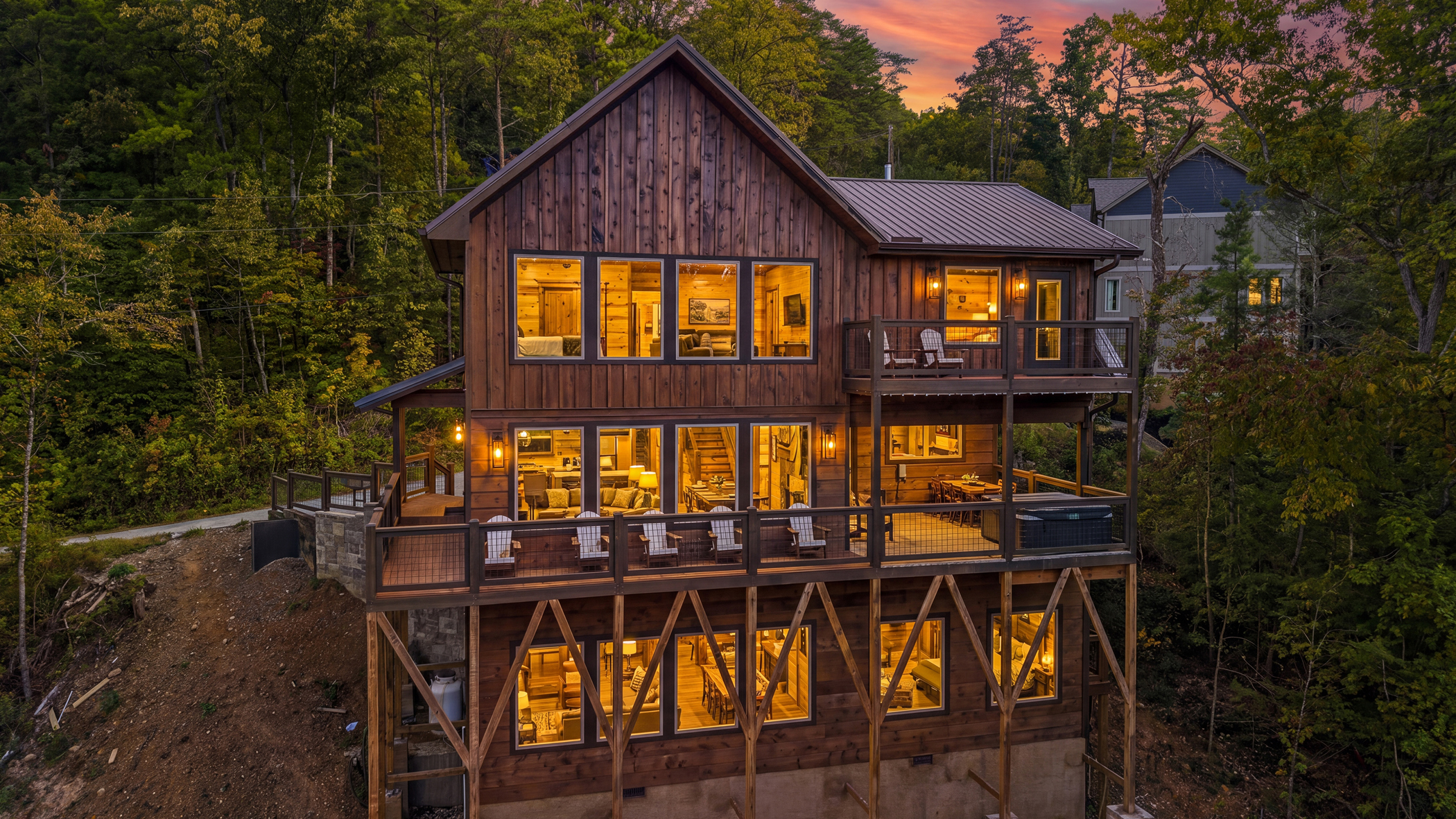 The rear decks and glowing windows of a three-level cabin at dusk.