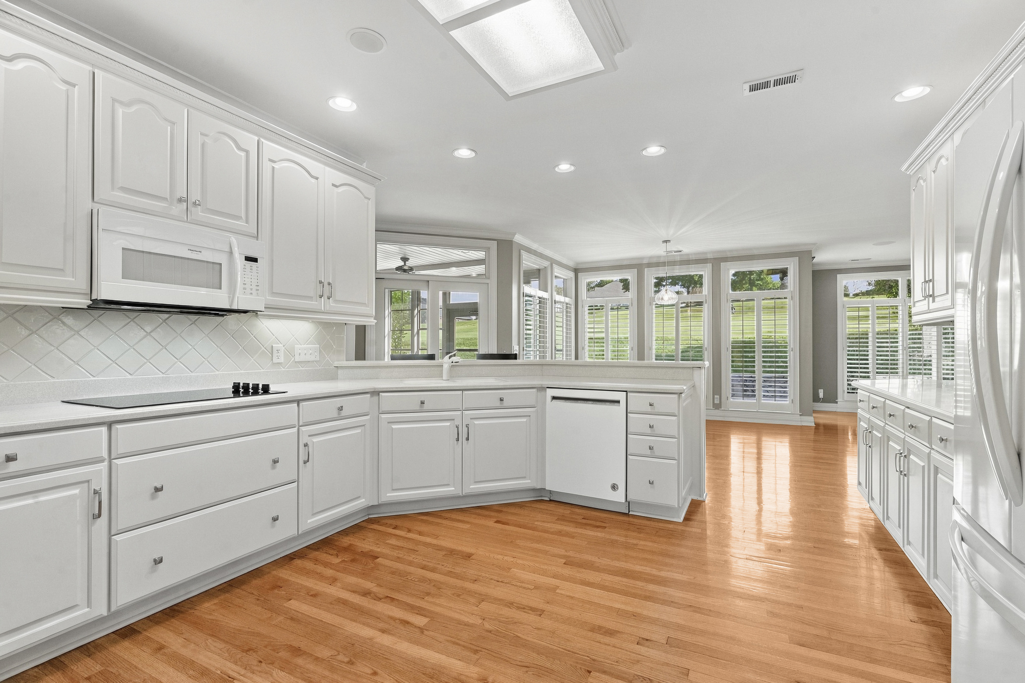 Bright white kitchen with warm wood floors and daylight through a wall of windows.