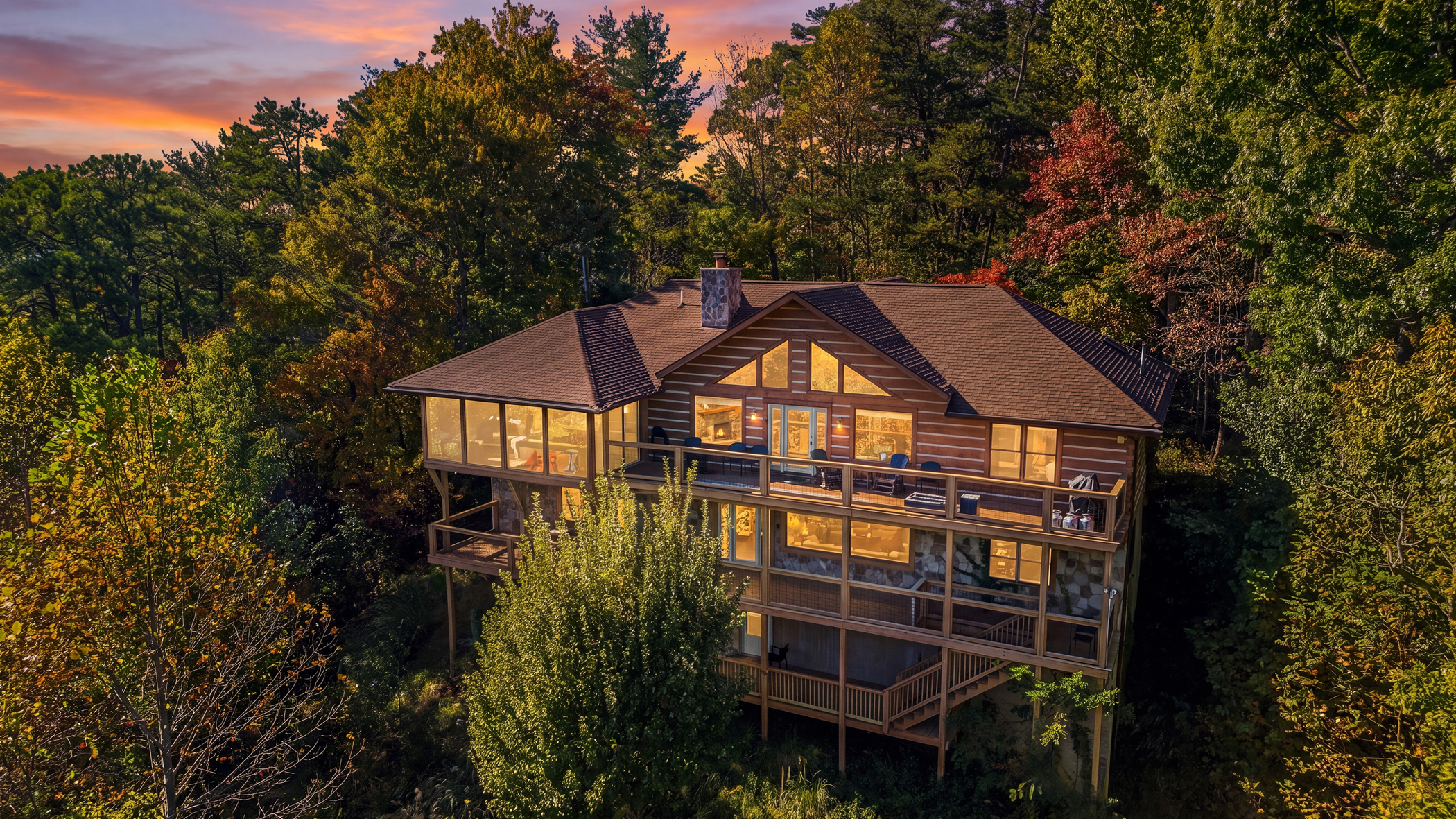 Illuminated Gatlinburg cabin surrounded by autumn trees beneath a glowing twilight sky.